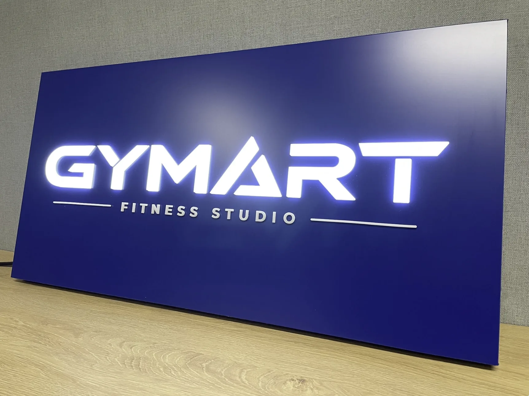 Modrá svetelná tabuľa s podsvietenými písmenami GYMART Fitness Studio — realizácia Neonworld